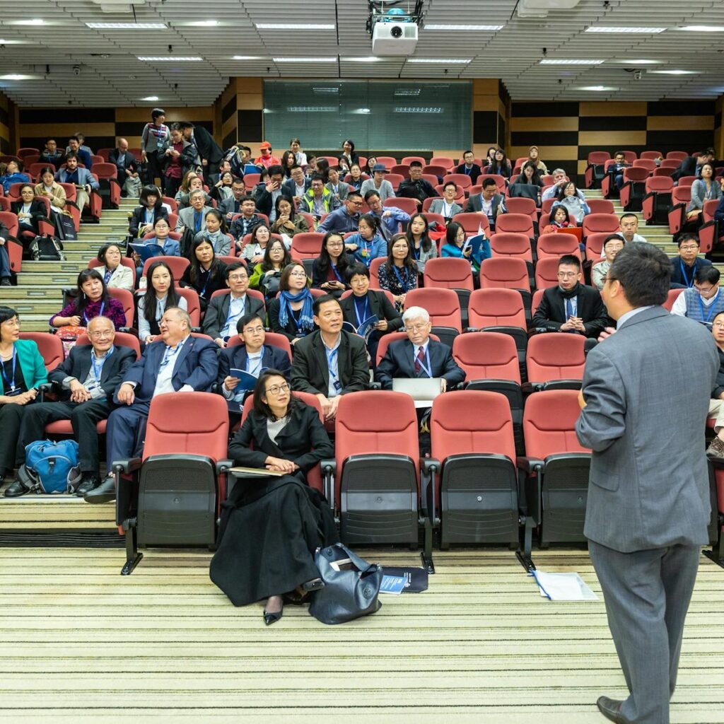 Professional setting of a business conference with attendees and a presenter in an auditorium.