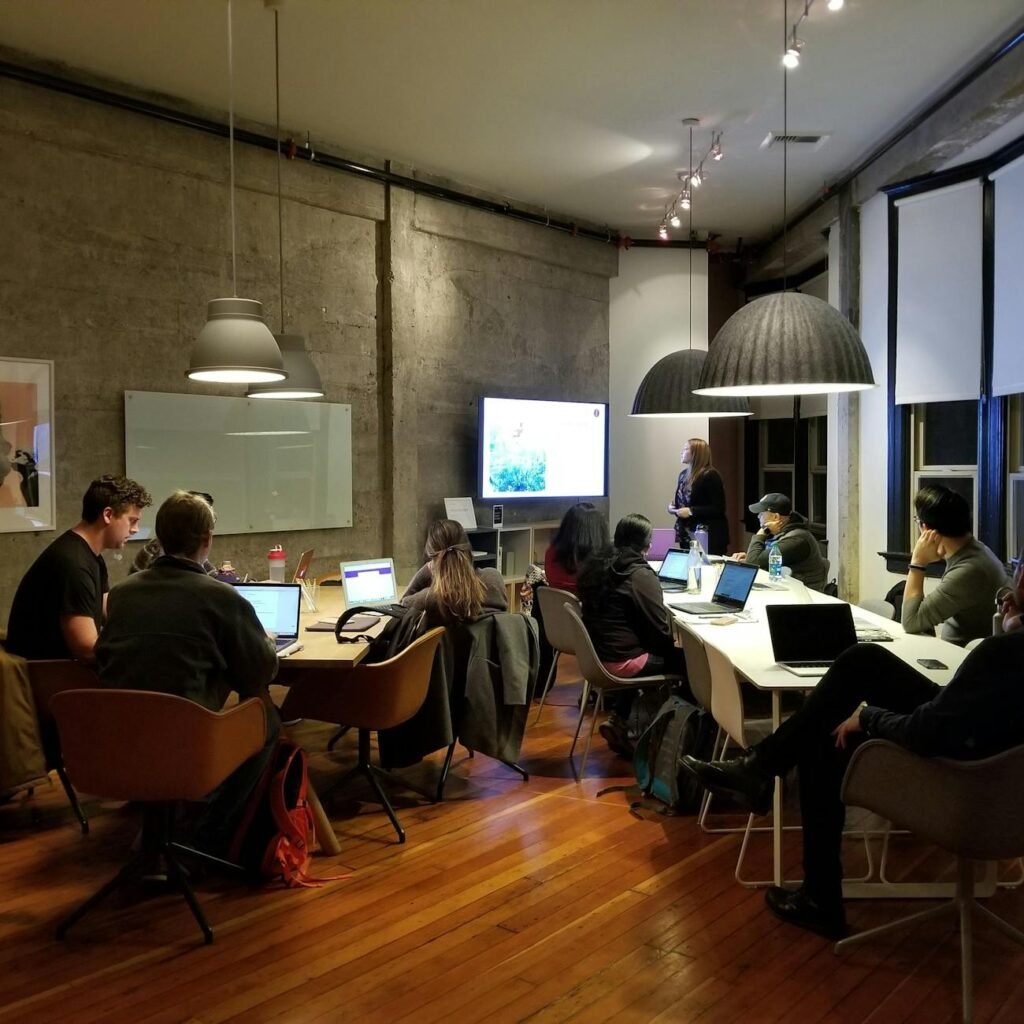 Diverse team collaborating in a modern office setting with laptops and presentation screen.